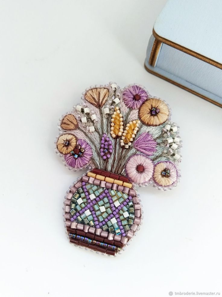 a beaded brooch with flowers in a vase on a table next to a purse