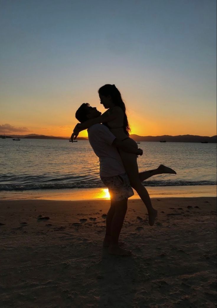 a man holding a woman on the beach at sunset