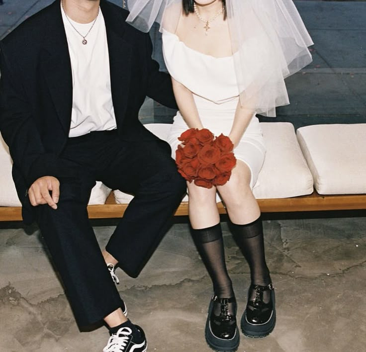 a man and woman sitting on a bench wearing wedding attire with veils over their heads