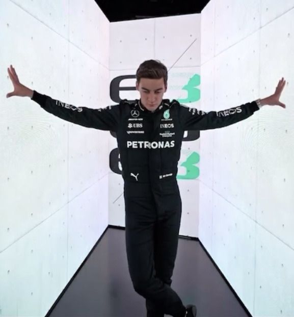 a young man in a black racing suit standing on a runway with his arms outstretched