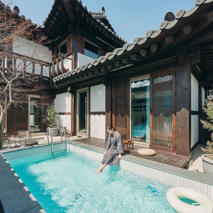 a man sitting on the edge of a swimming pool in front of a building with an open door