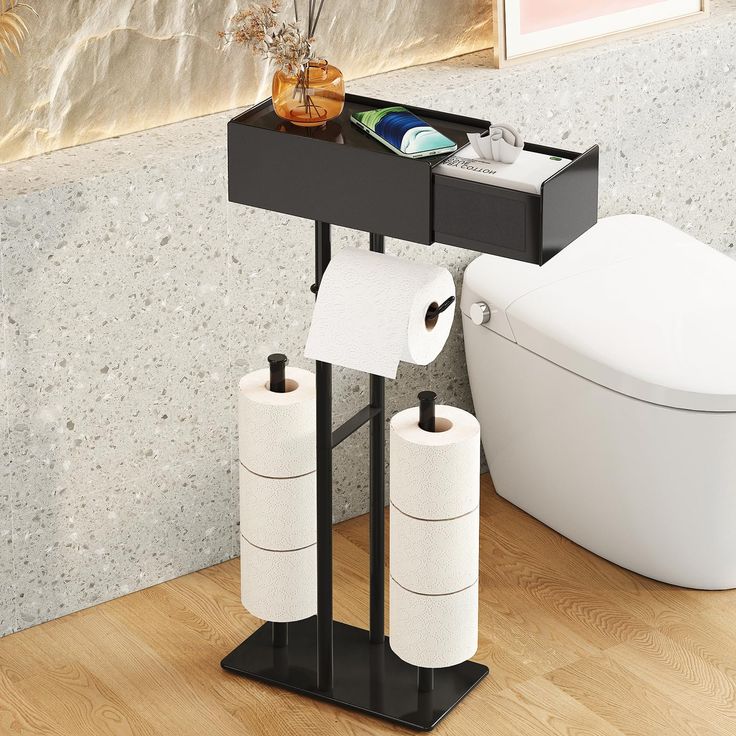 two rolls of toilet paper sitting on top of a black stand next to a toilet