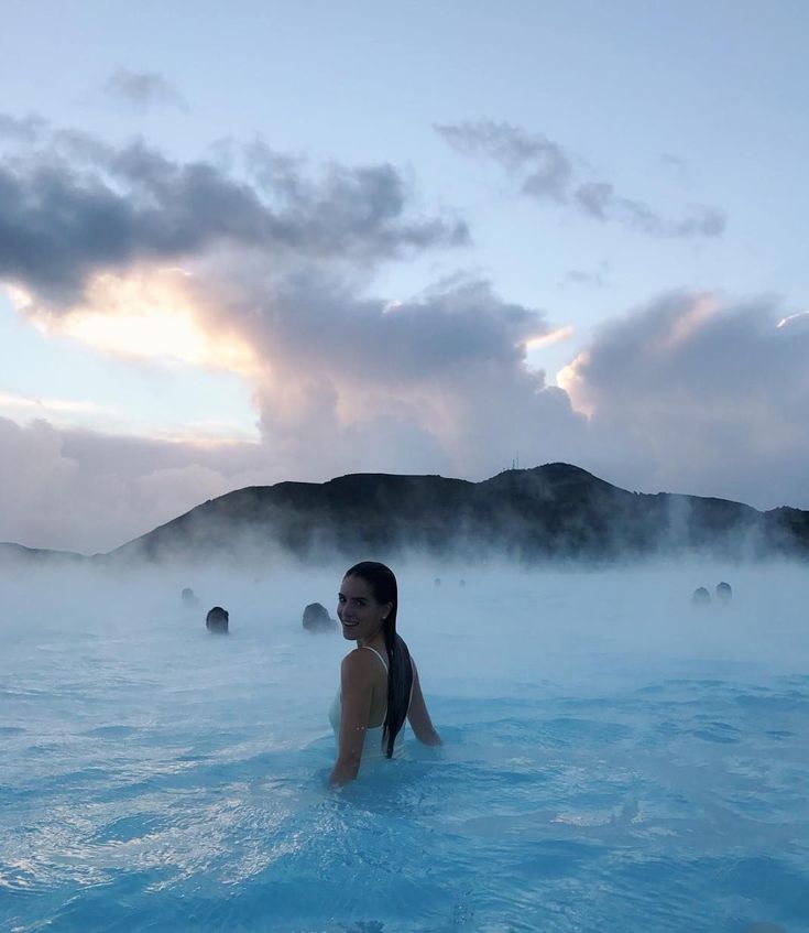 a woman sitting in the middle of a body of water with steam rising from it