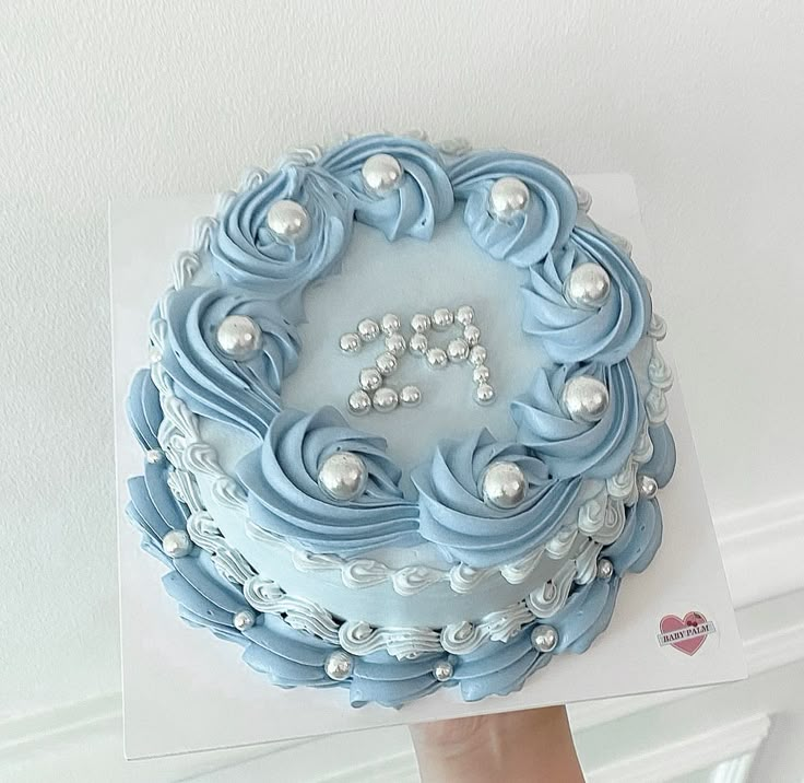 a person holding up a blue frosted cake with pearls on the top and bottom