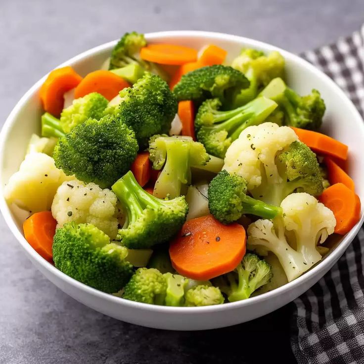 a bowl filled with broccoli and carrots on top of a checkered table cloth