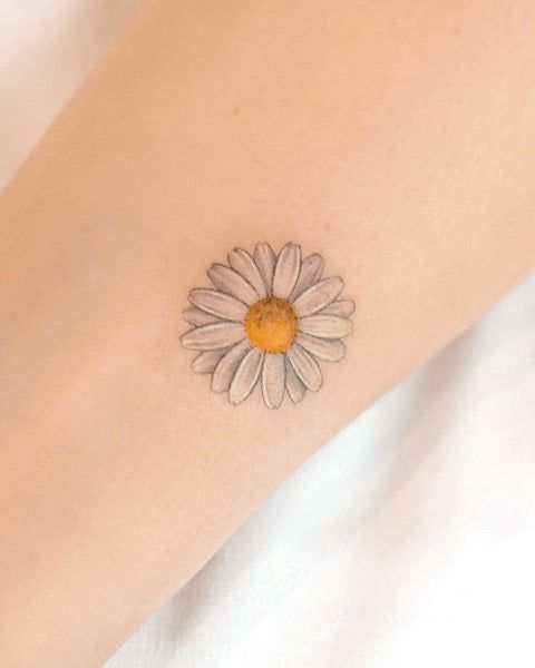 a woman's arm with a small daisy tattoo on the left side of her arm