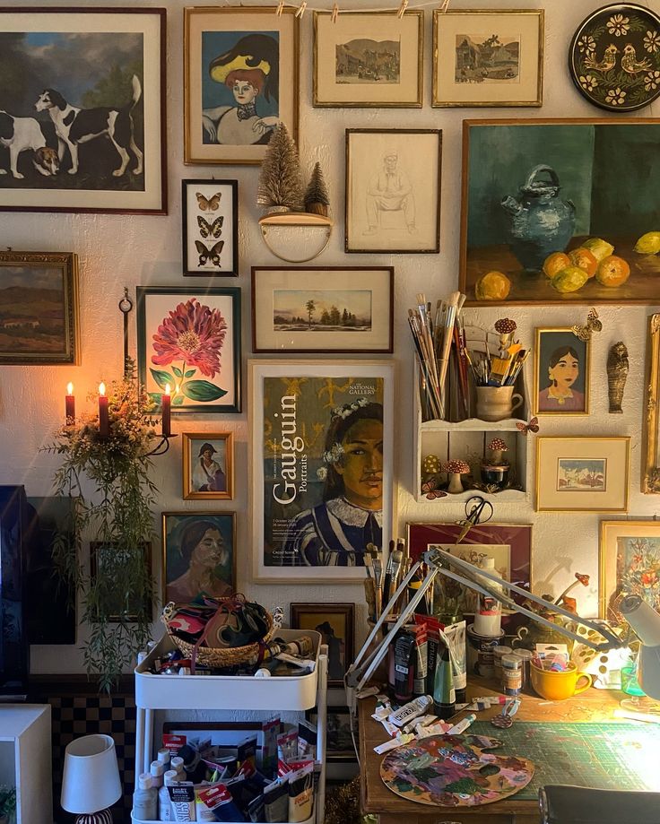 a room filled with lots of framed pictures and paintings on the wall next to a desk