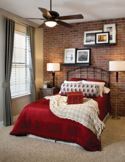 a bedroom with a brick wall and red bedding, two framed pictures on the wall