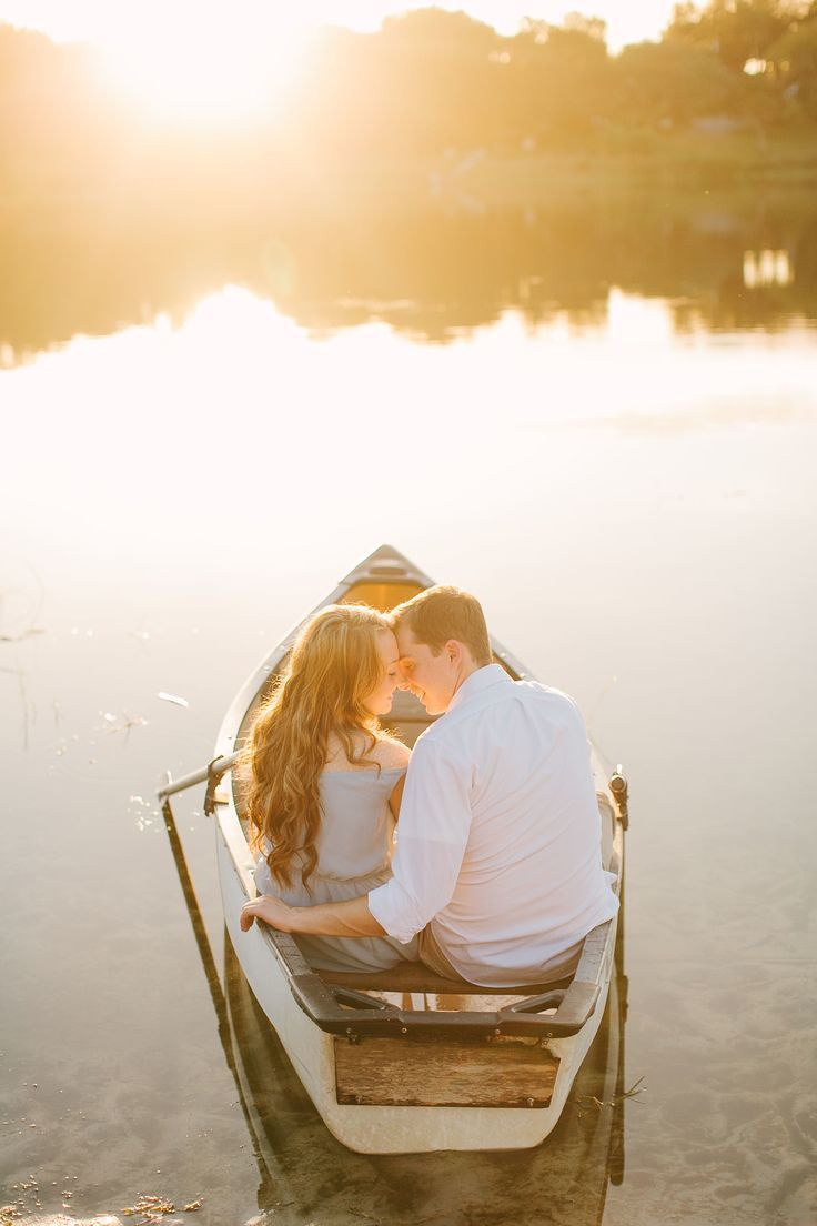 a man and woman sitting in a small boat on the water with their faces close to each other