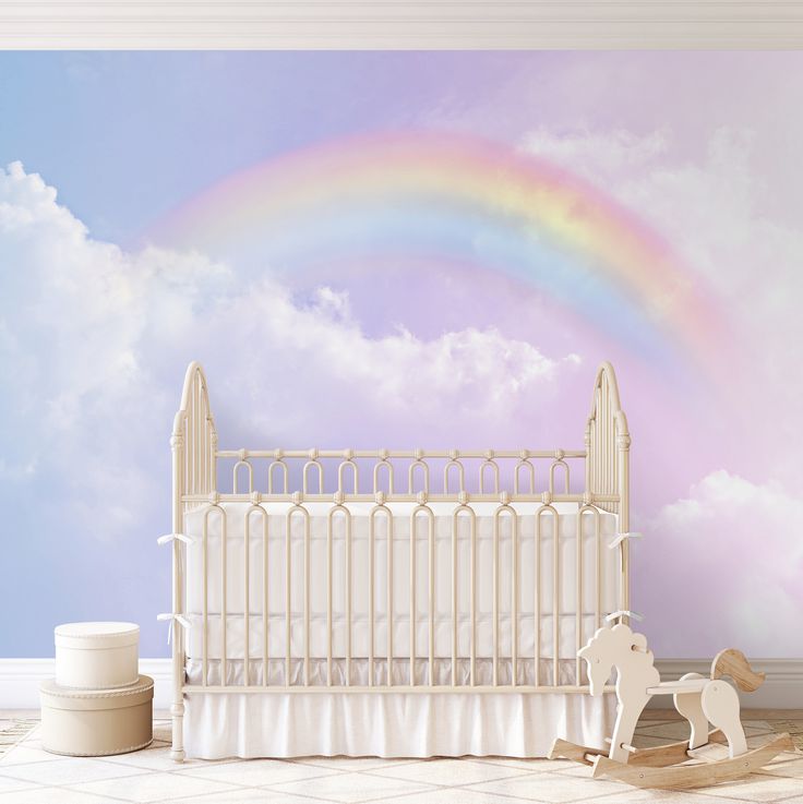 a white crib with a rainbow painted on the wall and clouds in the background