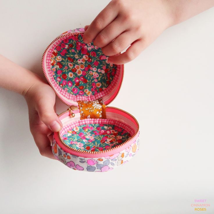 two hands are holding small pink and green tins with flowers on them, one has a gold ring in it