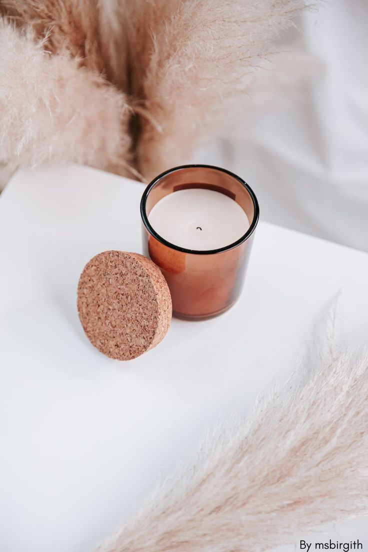 a candle sitting next to a round cork coaster on top of a white table cloth