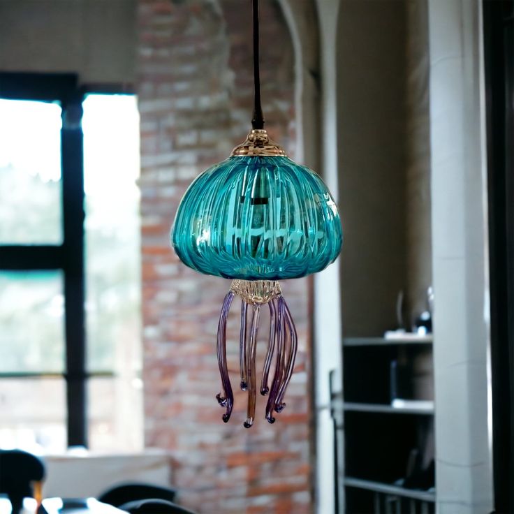 a blue glass light hanging from a ceiling in a room with brick walls and windows