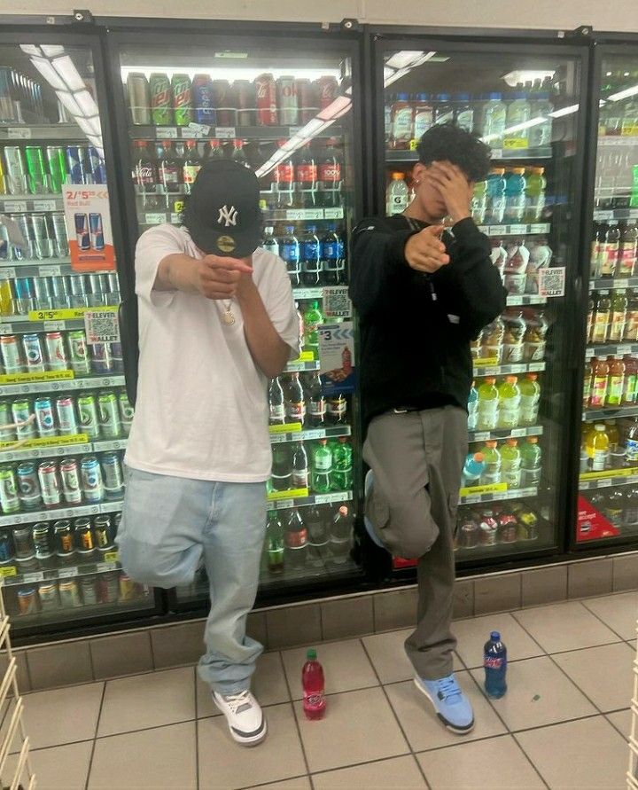 two young men standing in front of a display of sodas and beer bottles, one holding his face to his mouth