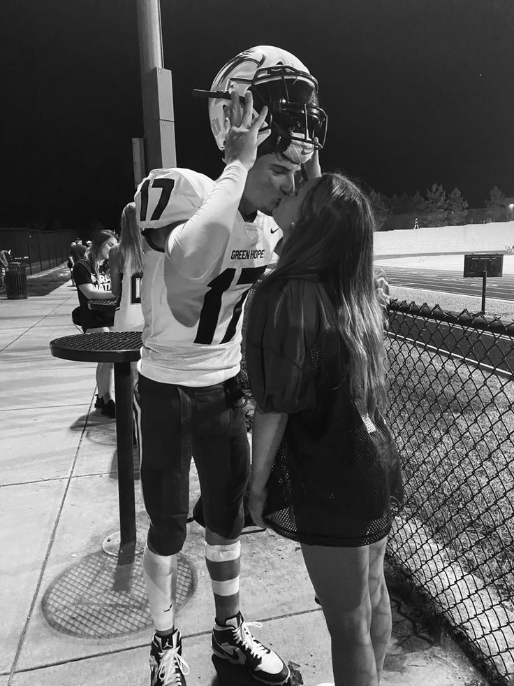 a man and woman standing next to each other near a fence with a football helmet on