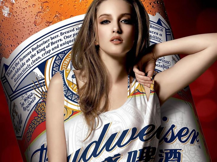 a beautiful young woman standing next to a bottle of budweiser beer in front of a red background