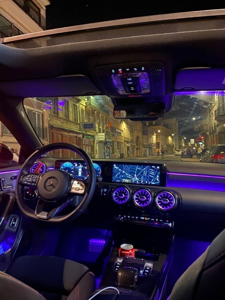 the interior of a car with blue lights and dashboard controls in front of a city street at night