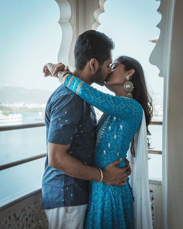 a man and woman kissing on the deck of a boat in front of some water