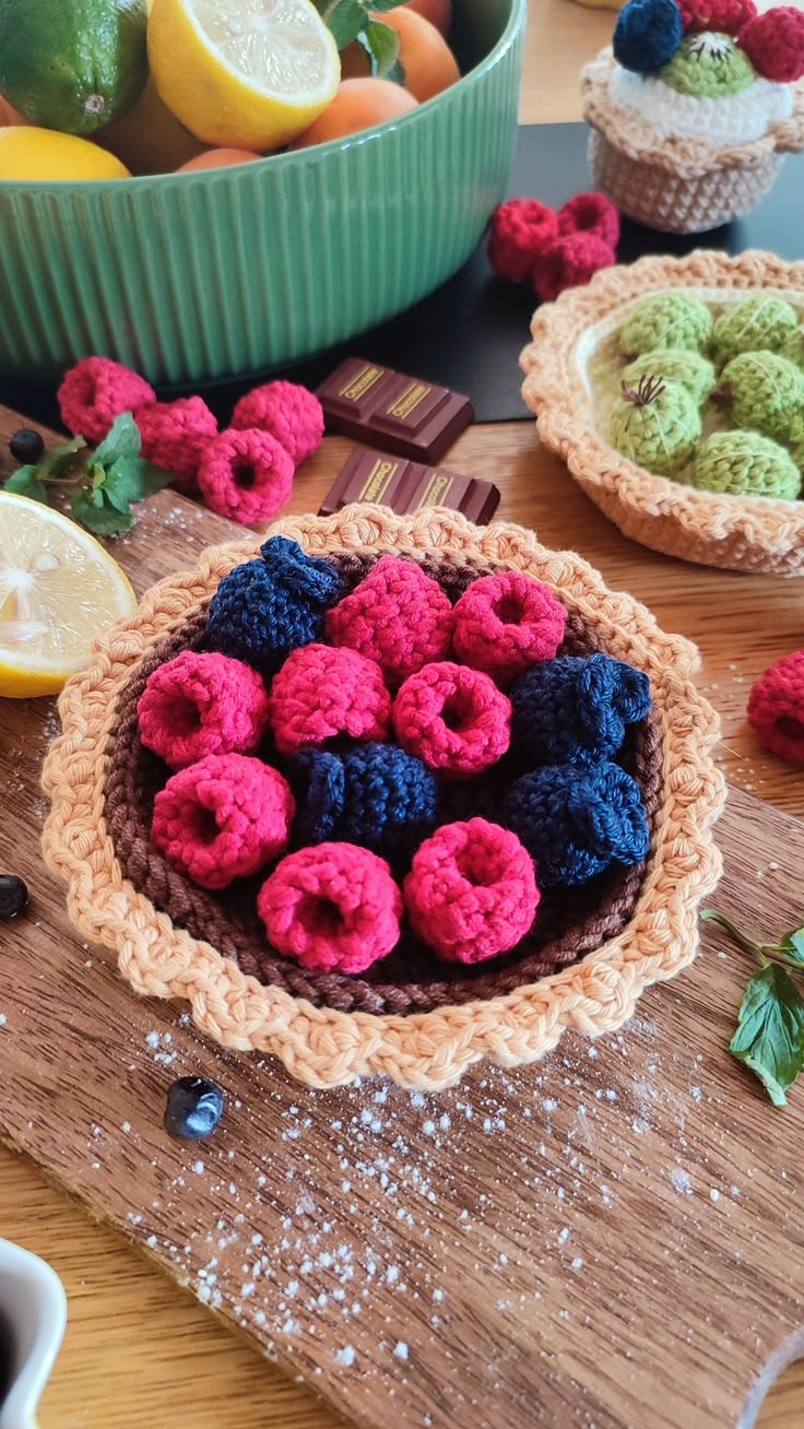 some crocheted fruits are sitting in bowls on a table next to lemons and raspberries