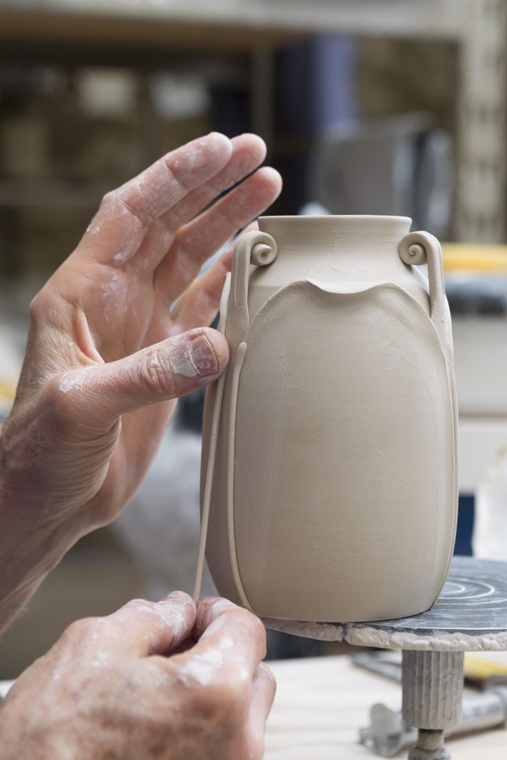 a person is making a vase out of clay with one hand and the other holding it