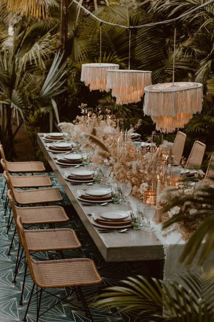 a long table is set with place settings and hanging chandeliers, surrounded by palm trees