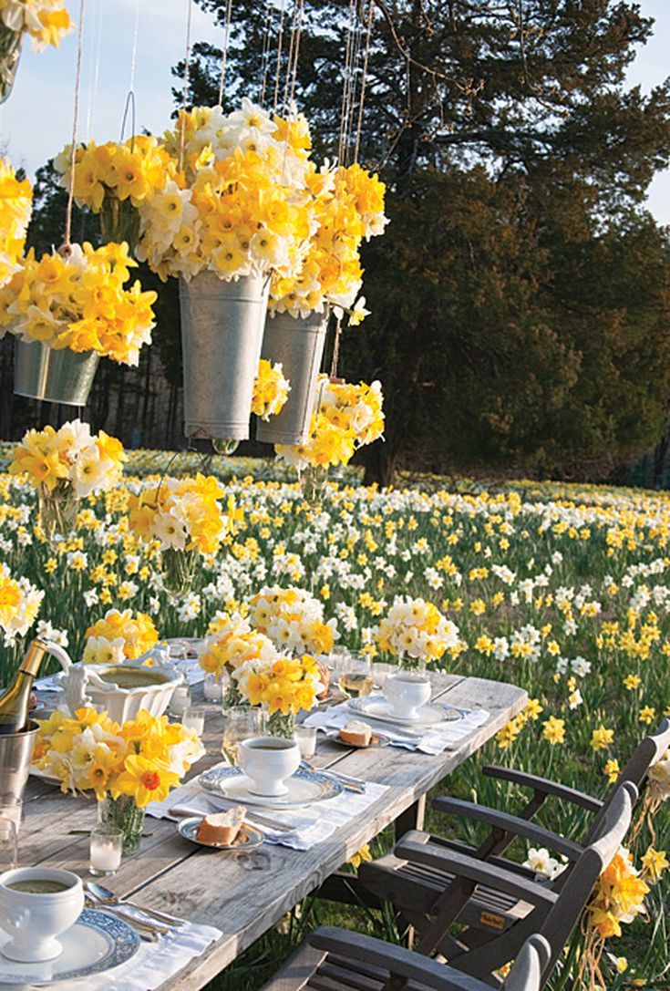 a picnic table with yellow and white flowers in hanging baskets on the back drop off chairs