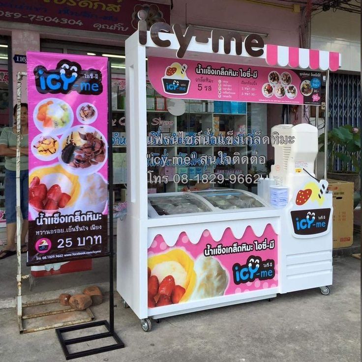 an ice cream stand in front of a store with pink and white signs on it