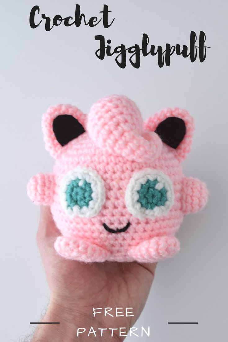 a hand holding a pink crocheted toy with eyes