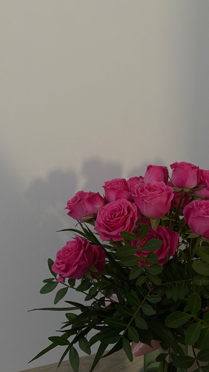 a vase filled with pink roses sitting on top of a wooden table next to a white wall