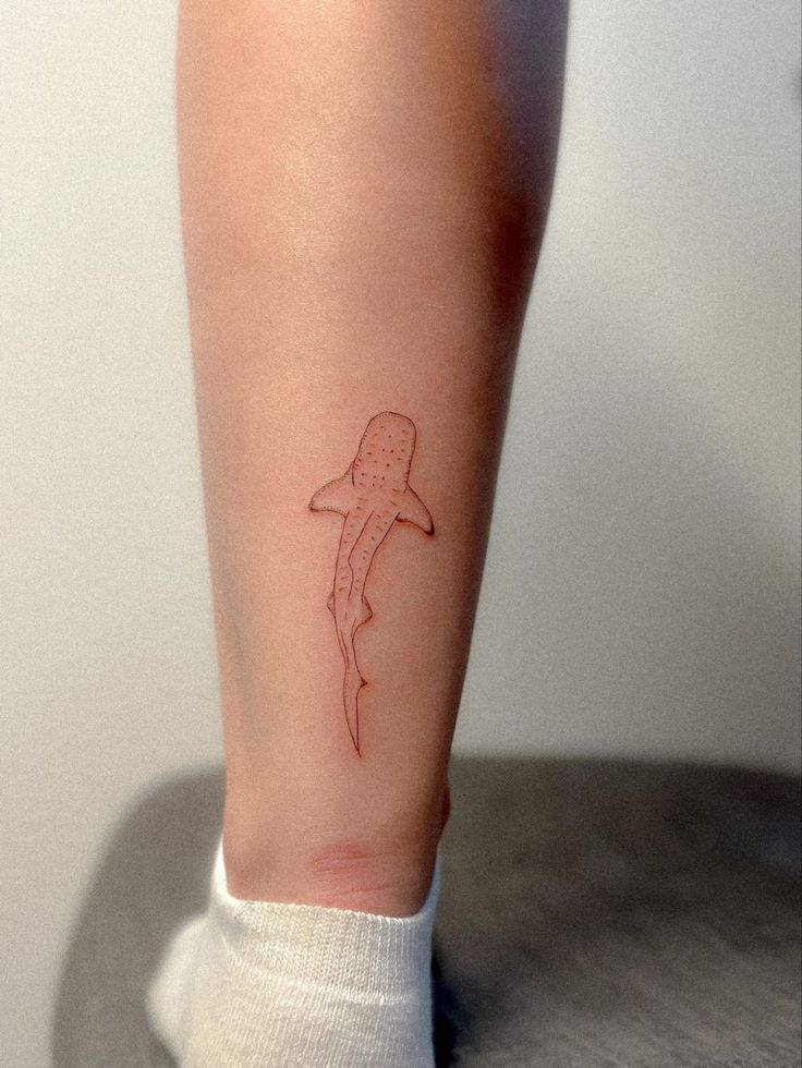 a small tattoo on the leg of a person's foot with a shark drawn on it