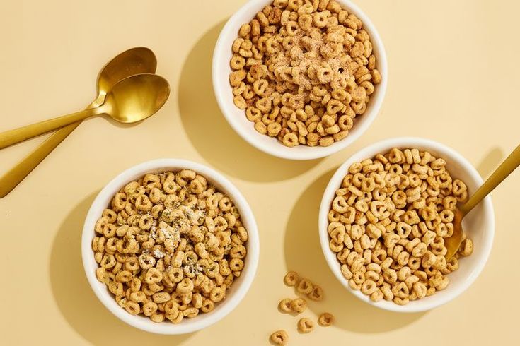 three bowls filled with cereal next to two spoons