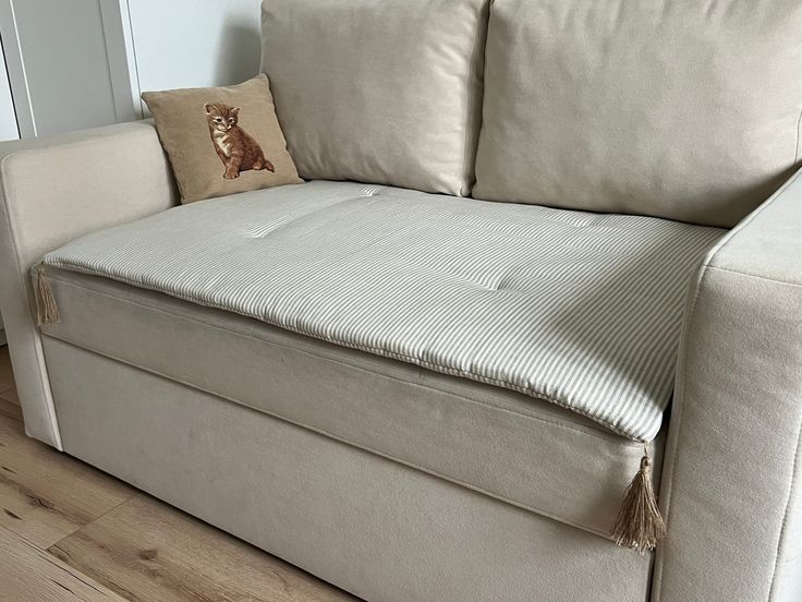 a white couch with two pillows on top of it and a cat pillow next to it