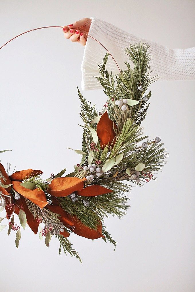 a person is holding a wreath with flowers and greenery in the middle of it