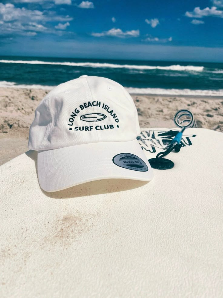 "Rep one of our favorite beach towns with this trendy hat!  This hat style features our Surf Club graphic and a low profile with an adjustable strap and curved visor. Perfect for those sunny beach days! This embroidered black and pink design comes in: Pink, Light Blue, Stone, Khaki, and White. Item Features: * 100% chino cotton twill * Unstructured, 6-panel, low-profile * 6 embroidered eyelets * 3 ⅛\" (7.6 cm) crown * Adjustable strap with antique buckle *Please note: Color may differ slightly from how it appears on your screen due to varying monitor settings.  Some designs may come with a white paper backing on the inside of the embroidered design, this is needed during the creation process to ensure the strength and longevity of the design. This product is made especially for you as soon Cheap Pink Baseball Cap For Beach, White Adjustable Hat For Vacation, Adjustable White Hat For Vacation, White Adjustable Sun Hat For Vacation, Summer Trucker Hat With Upf 50+ And Curved Brim, White Adjustable Summer Sun Hat, White Beach Hat For Travel, White Trucker Hat For Beach Season Vacation, White Hat For Poolside Vacation