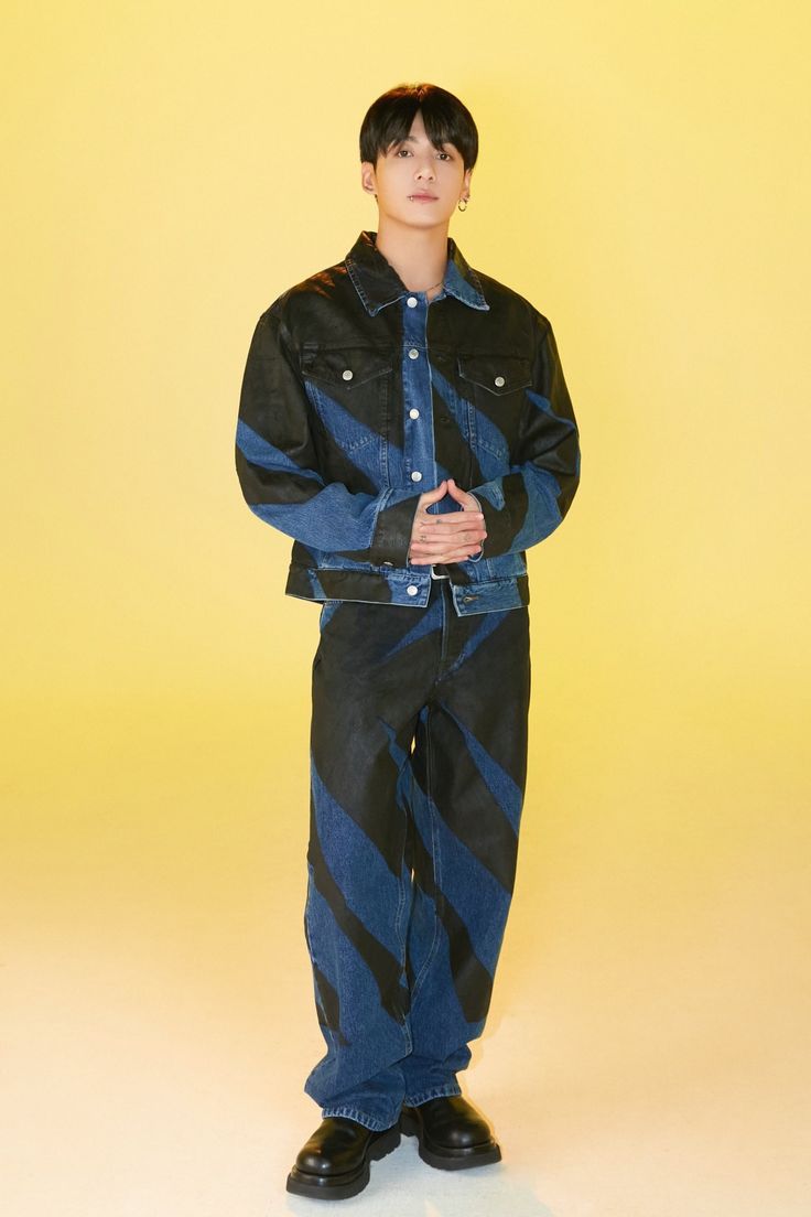 a young man standing in front of a yellow background wearing black and blue striped pants