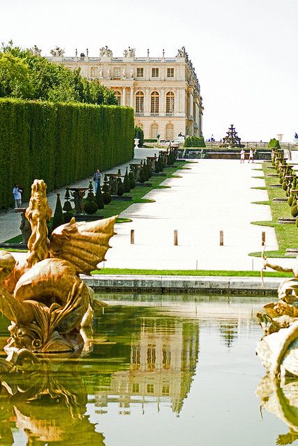 an elaborate fountain in the middle of a garden with trees and hedges around it,