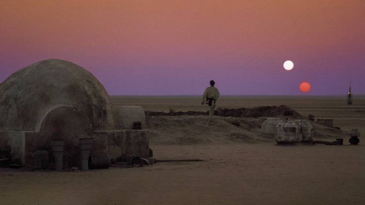 a man standing on top of a sandy field next to a large object in the distance