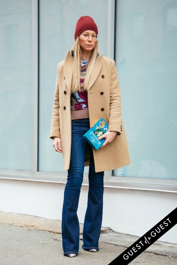 a woman standing in front of a building with her hand on her hip wearing a coat and jeans