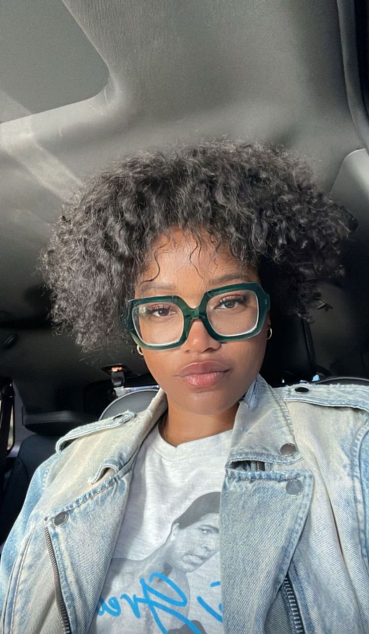 a woman with glasses sitting in the back seat of a car looking at the camera