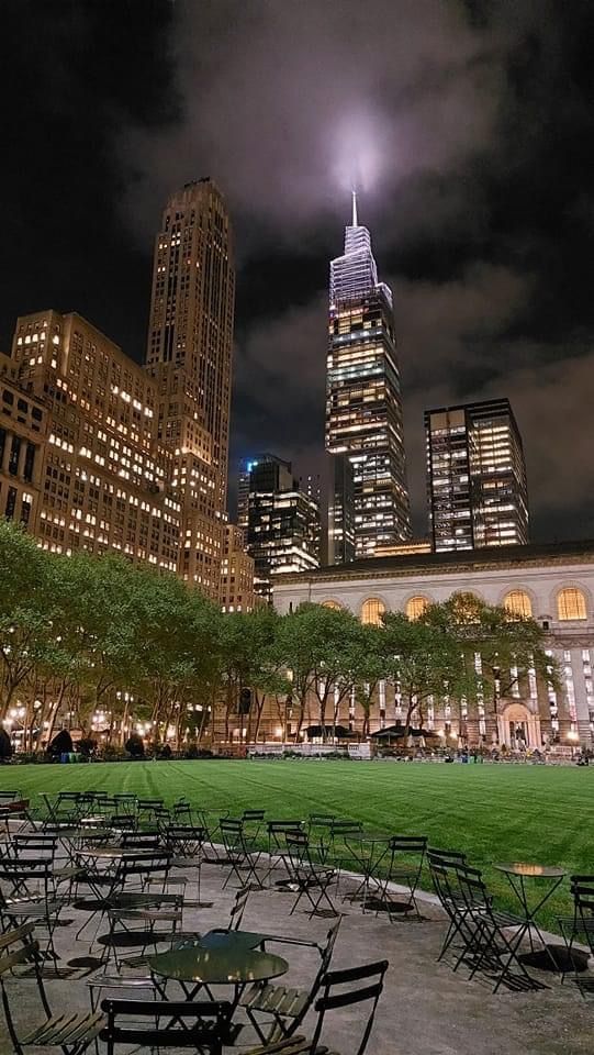 tables and chairs are set up on the grass in front of tall buildings at night