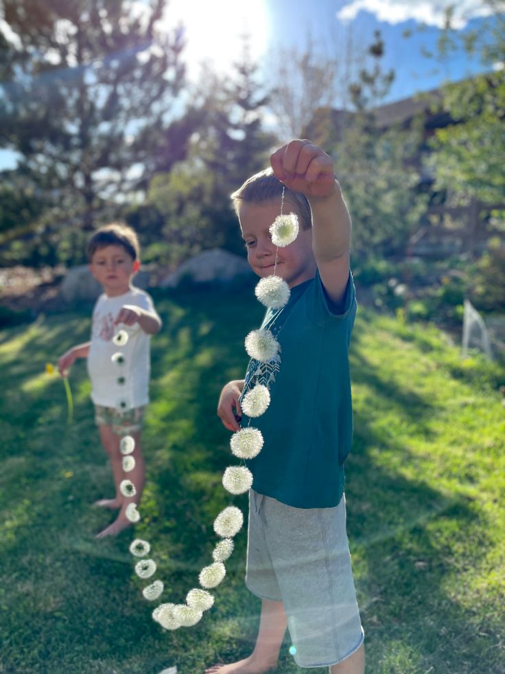 two young boys standing in the grass playing with paper flowers and streamers on a string