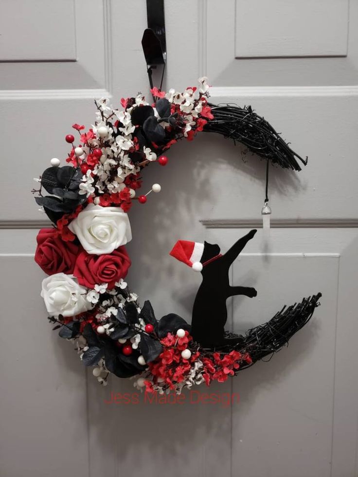 a wreath is hanging on the door with red and white flowers, black ribbon, and a santa's hat