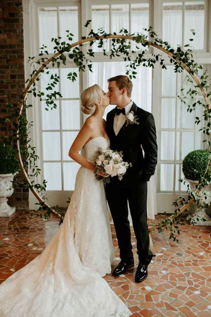 a bride and groom standing in front of an arch with greenery on it at their wedding