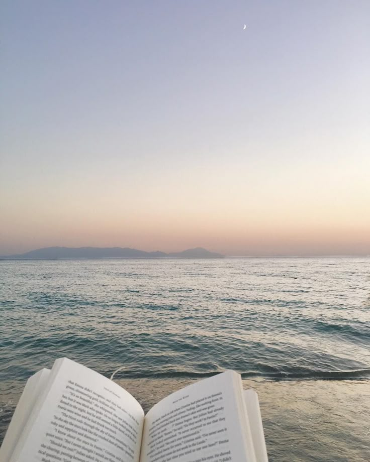 an open book sitting on top of a beach next to the ocean