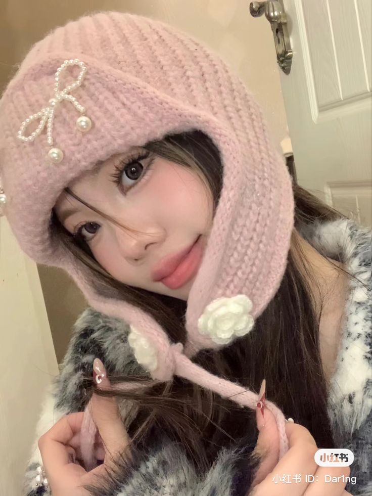 a girl with long hair wearing a pink hat and holding a pair of scissors in front of her face