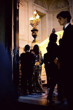 several people standing in front of a large golden structure with chandeliers on it