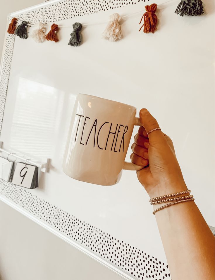 a person holding a coffee mug with the word teacher on it