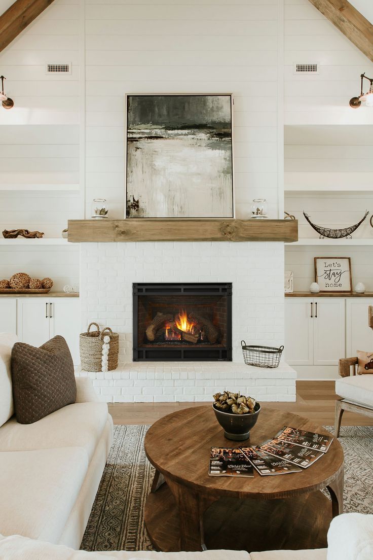 a living room with white furniture and a fire place in the middle of the room