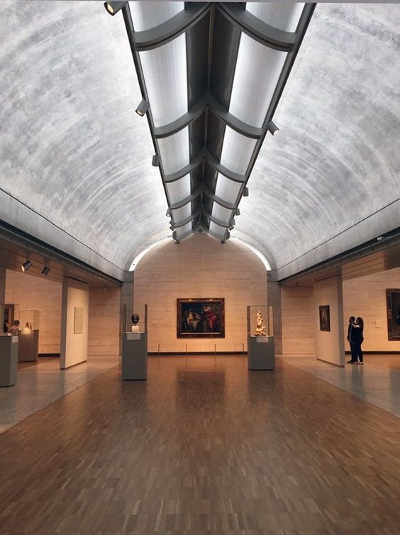 an empty room with paintings on the walls and people standing in the distance looking at them