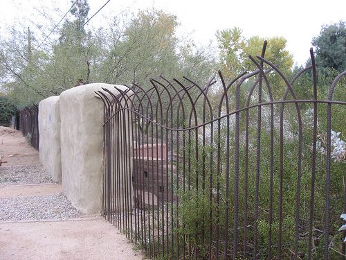 an iron fence is next to a stone wall and shrubbery in the foreground